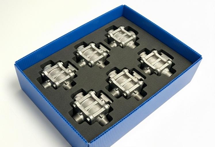 Seis válvulas metálicas industriales organizadas en una caja azul de polipropileno con inserto de espuma técnica negra para protección en transporte.
